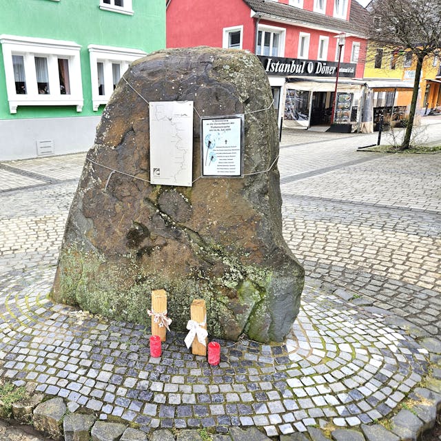 Das Foto zeigt einen großen Stein mit zwei kleinen Schildern und zwei Kerzen.