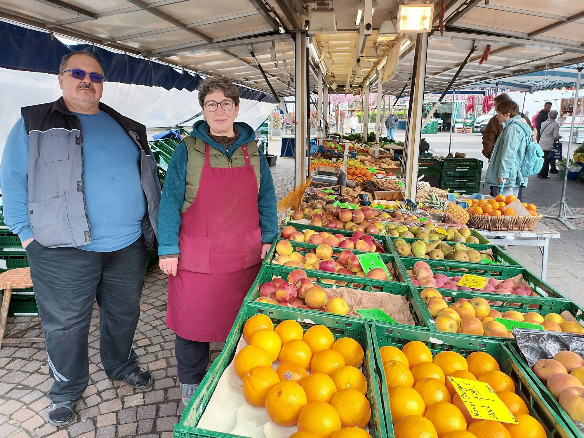 Eine Frau und ein Mann hinter einem Marktstand mit Obst