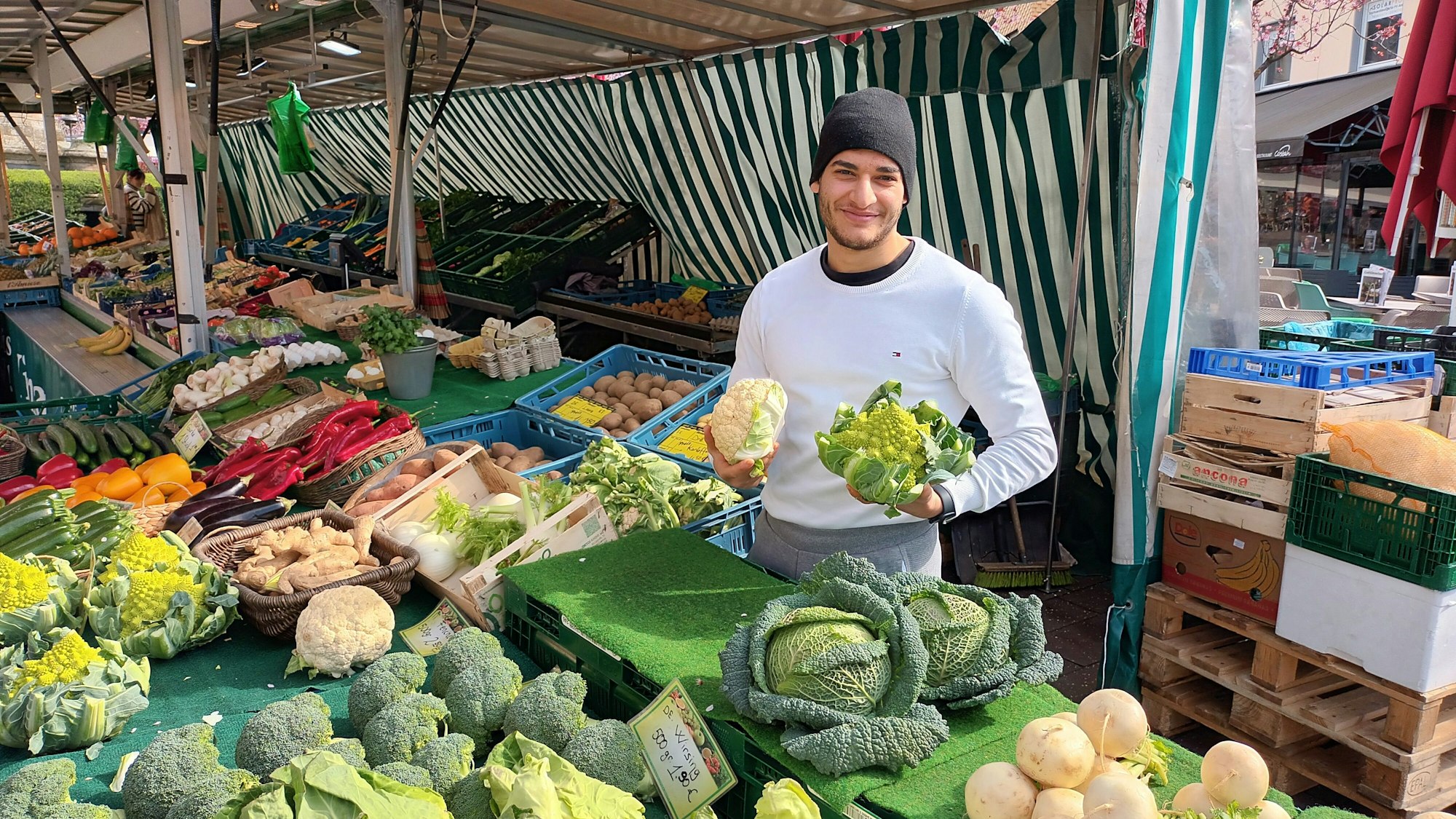 Mann an einem Marktstand mit Gemüse in der Hand