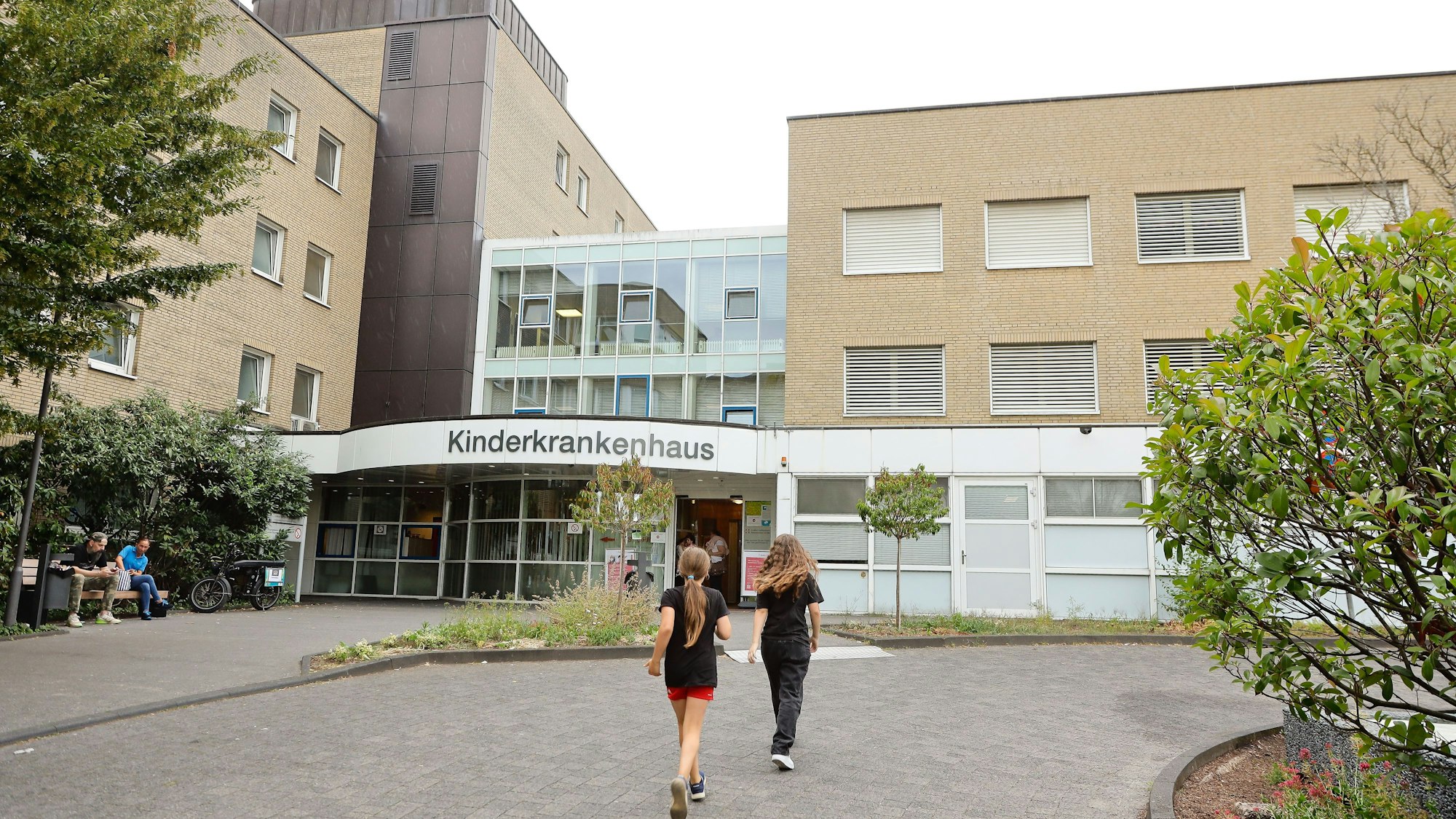 Das Bild zeigt ein Krankenhaus und Menschen vor dem Eingang.