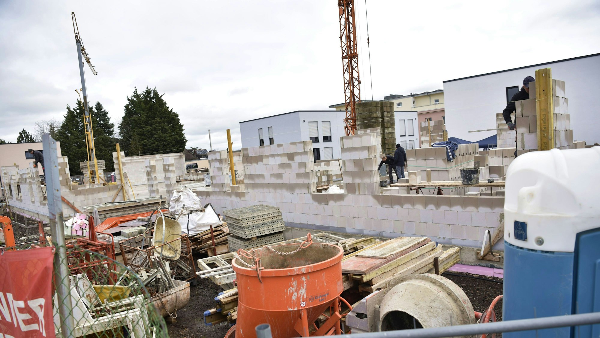 Das Bild zeigt eine Baustelle. Vor den ersten Mauern eines Gebäudes stehen Arbeitsmaterialien und ein Betonmischer.