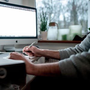 Ein Mann arbeitet im Home Office, vor ihm steht ein Laptop und ein großer Bildschirm.