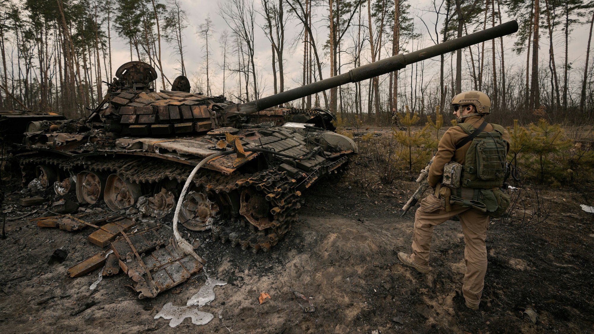 Ein ukrainischer Soldat steht neben einem zerstörten Panzer.
