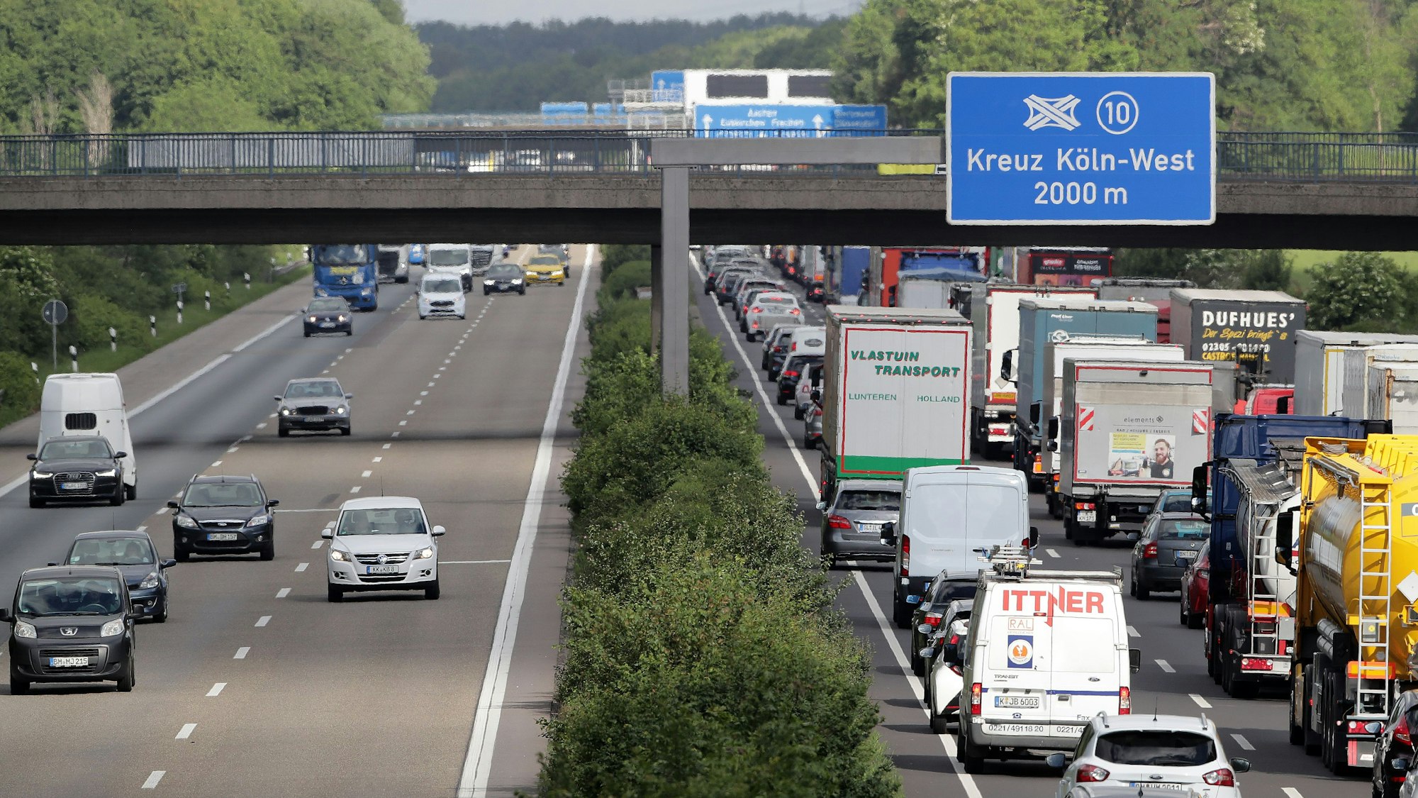 Verkehr auf der Autobahn, an einer Brücke hängt ein Schild mit der Aufschrift „Kreuz Köln-West 2000 m“.