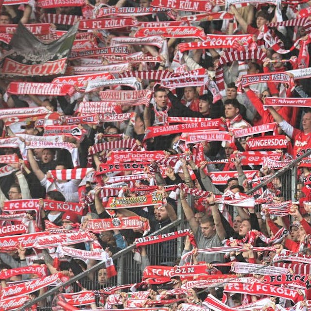 Fans des 1. FC Köln halten ihre rot-weißen Schals in die Höhe.