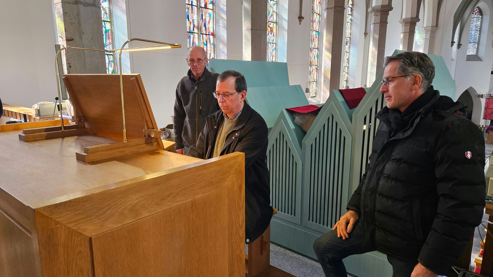 Karl-Wilhelm Jansen und Frank Weimbs stehen neben dem Spieltisch, an dem Organist Andreas Warler sitzt und spielt.