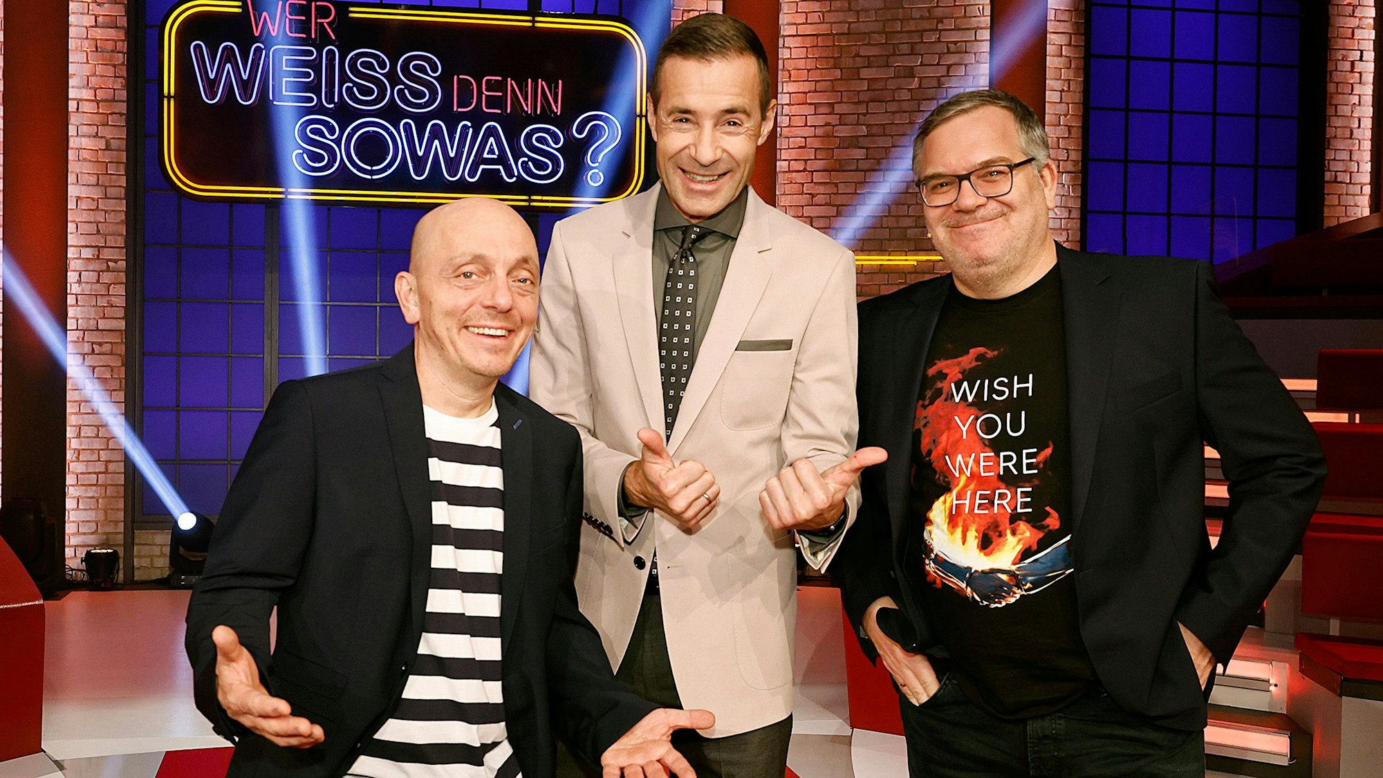Moderator Kai Pflaume (M.) steht gemeinsam mit Elton (rechts) und Bernhard Hoëcker vor dem Logo der ARD-Quizshow „Wer weiß denn sowas?“.
