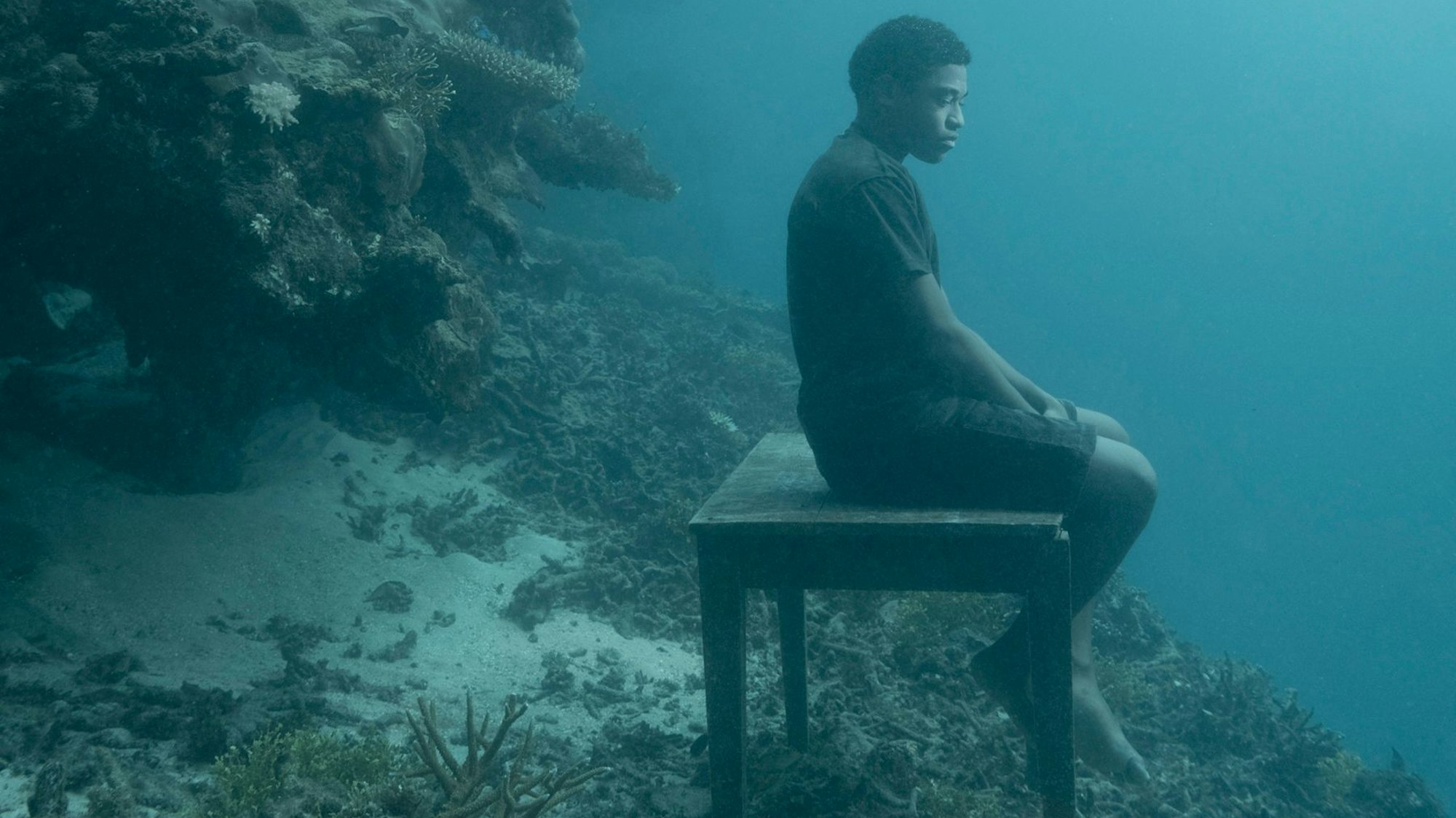 Ein Mann sitzt auf einem Tisch, der am Rande eines Abgrunds unter der Meeresoberfläche auf dem Meeresgrund steht.