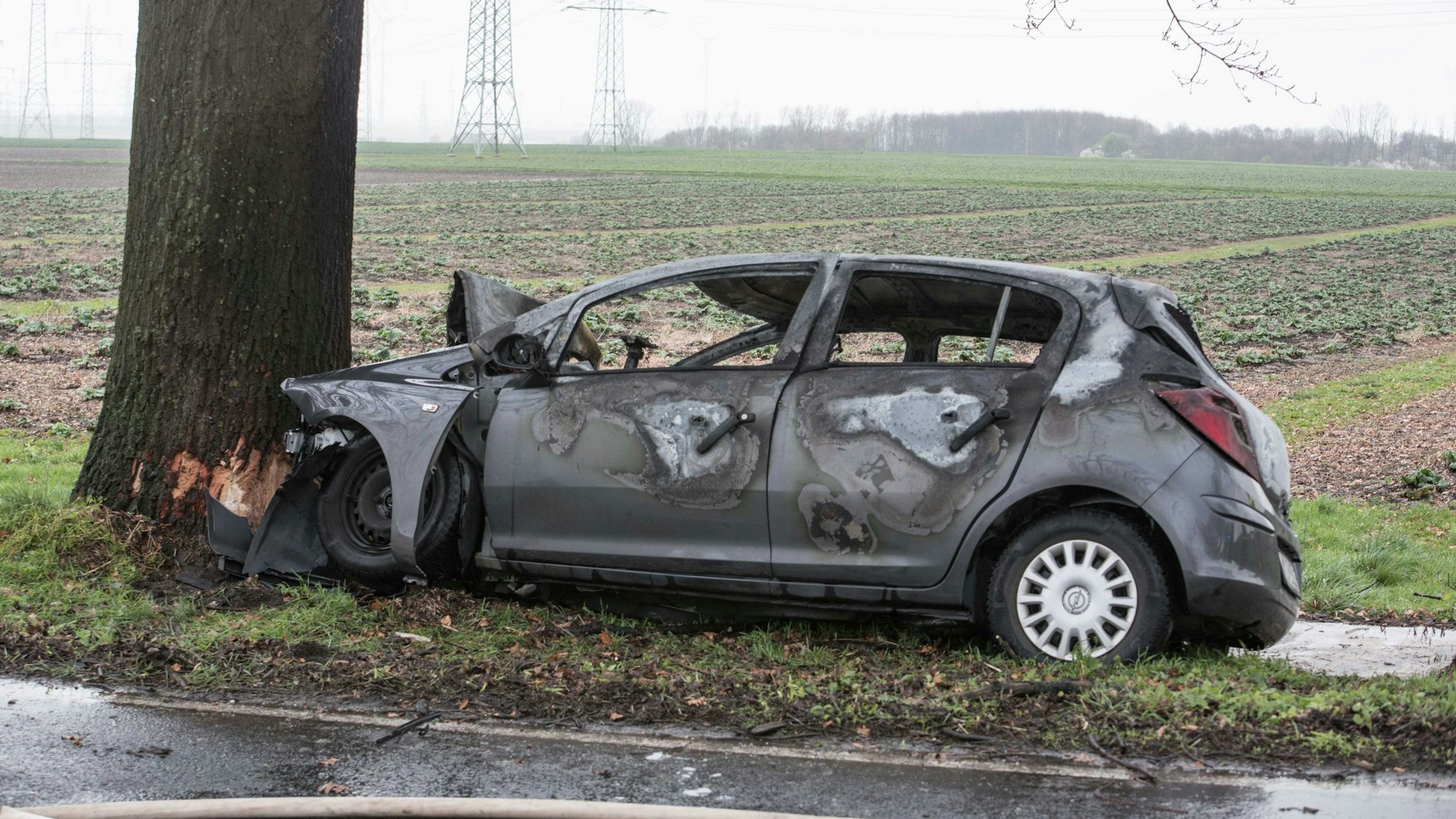 Foto eines zerstörten Autos, das gegen einen Baum geprallt ist und Feuer gefangen hat. Der Fahrer ist kurz darauf verstorben.