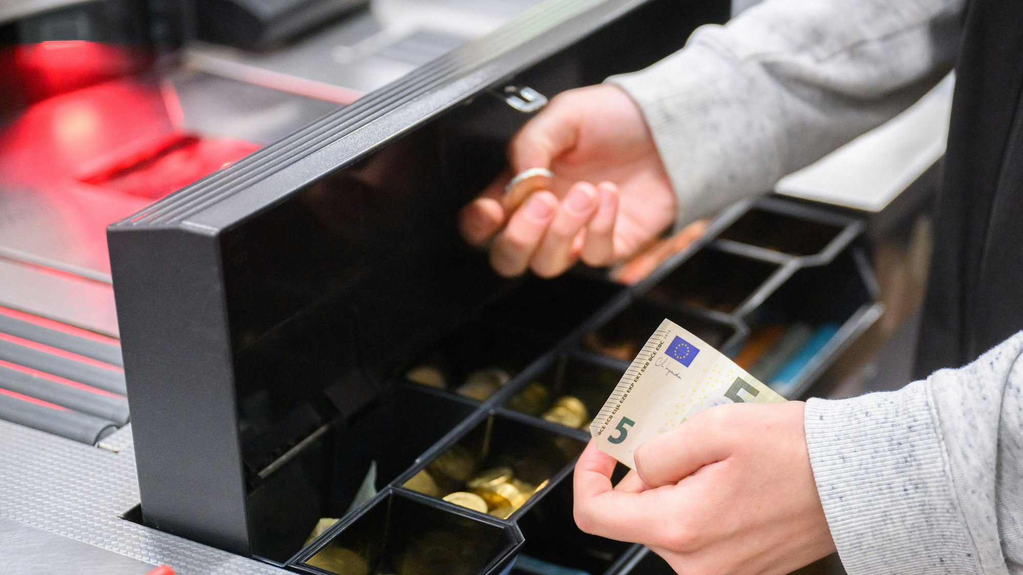 Eine Kassiererin nimmt Wechselgeld aus der Kasse eines Supermarktes.