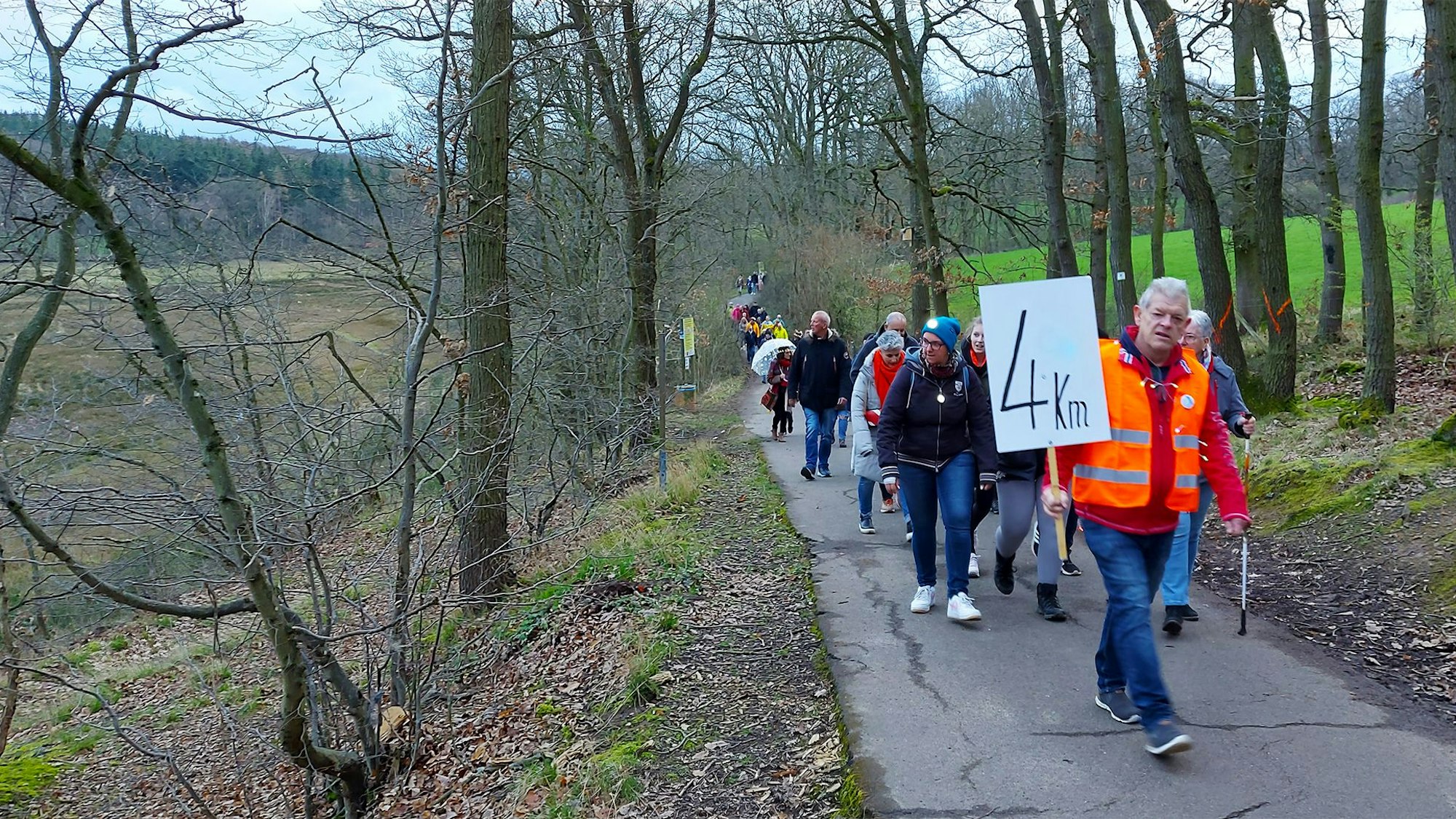 Hans Roitzheim, in orangefarbener Warnweste, trägt ein Schild mit der Aufschrift „4 km“. Ihm folgen mehrere Demoteilnehmer.