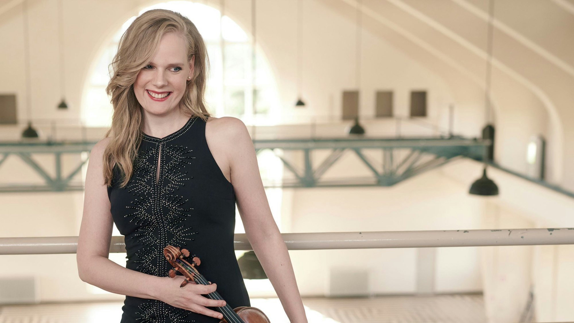 Simone Lamsma steht mit Geige in einer leeren Halle.