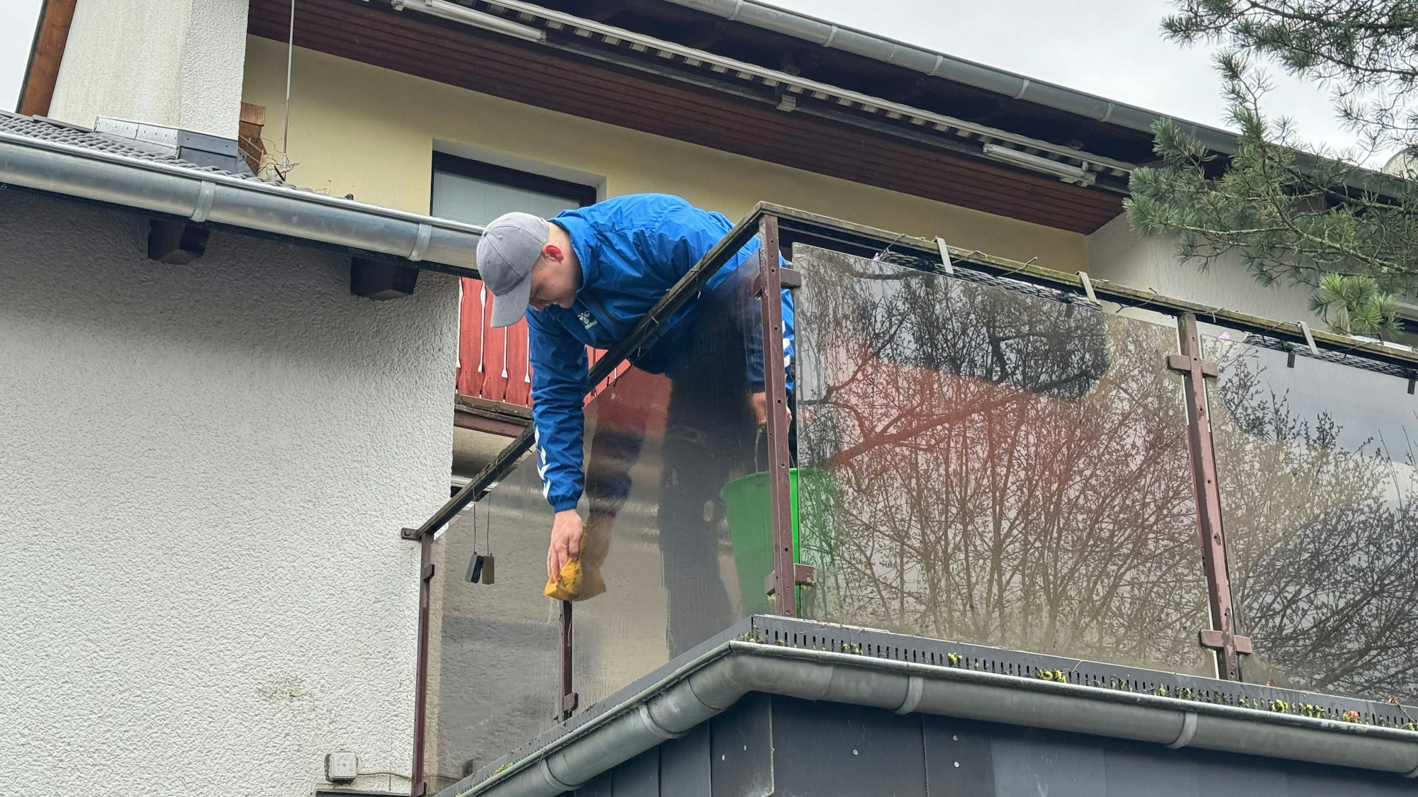 Ein Mann putzt die Brüstung eines Balkons mit einem Schwamm.