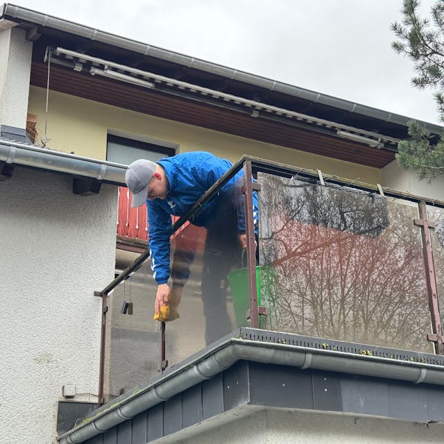 Ein Mann putzt die Brüstung eines Balkons mit einem Schwamm.