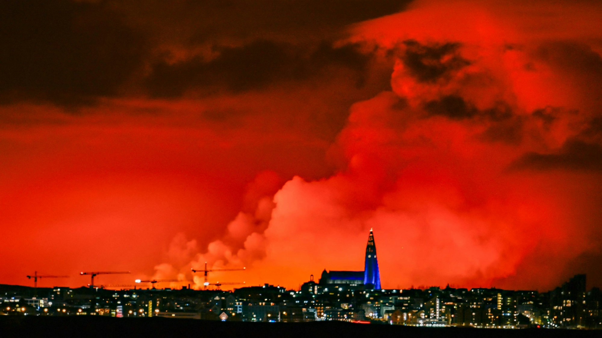 Die Skyline von Reykjavik ist vor dem Hintergrund eines orangefarbenen Himmels zu sehen, der durch geschmolzene Lava entstanden ist, die am 16. März 2024 aus einer Spalte auf der Halbinsel Reykjanes nördlich der evakuierten Stadt Grindavik im Westen Islands ausströmt.
