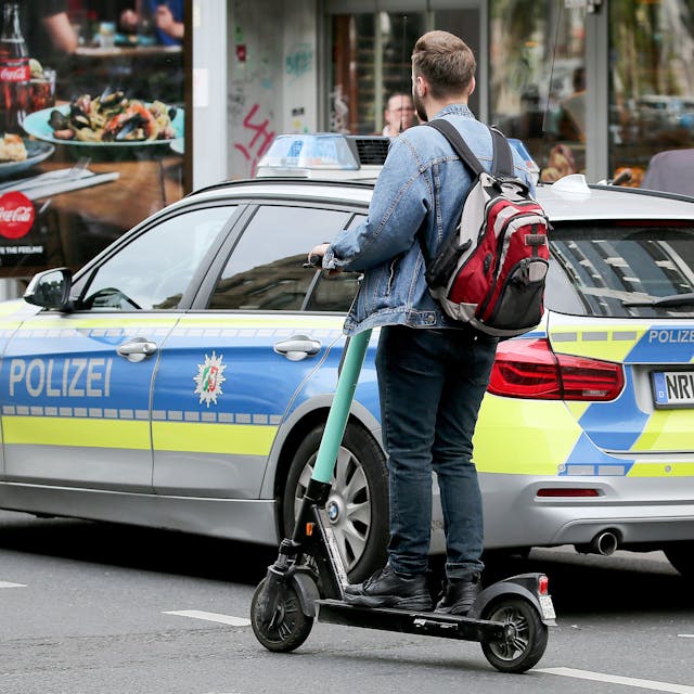 Ein Mann fährt mit einem E-Scooter an einem Polizeiauto vorbei.&nbsp;