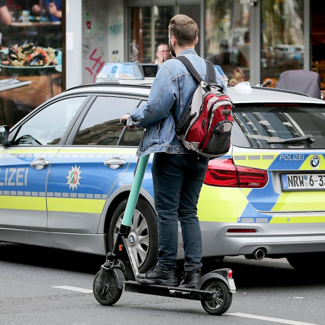 Ein Mann fährt mit einem E-Scooter an einem Polizeiauto vorbei.&nbsp;