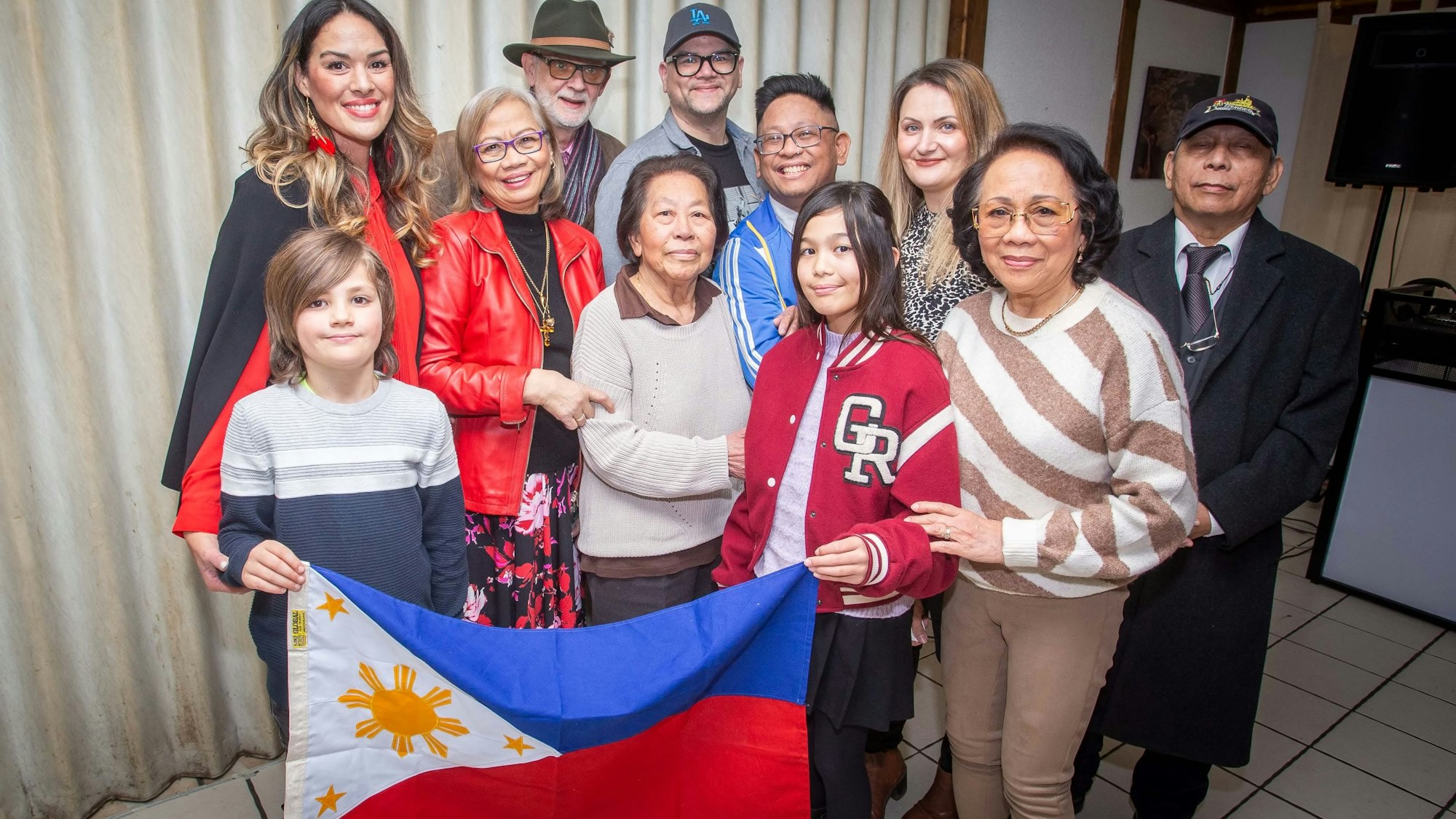 Mehrere Frauen und Männer stehen als Gruppe zusammen und halten die Flagge der Philippinen in den Händen.