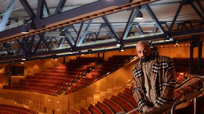 Xatar steht im leeren Zuschauerraum der Kölner Philharmonie. Er trägt ein helles kariertes Jackett.