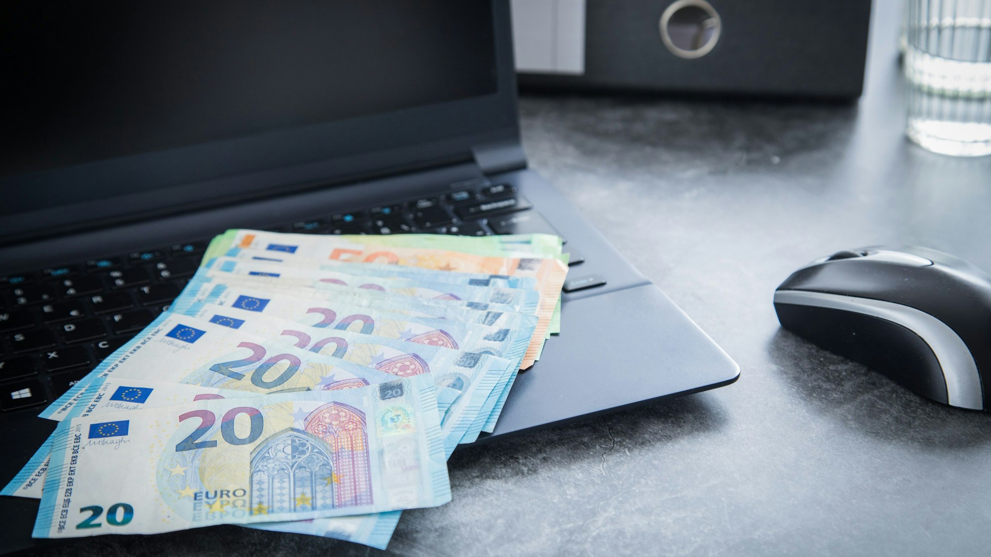 Euroscheine liegen aufgefächert auf der Tastatur eines Laptops