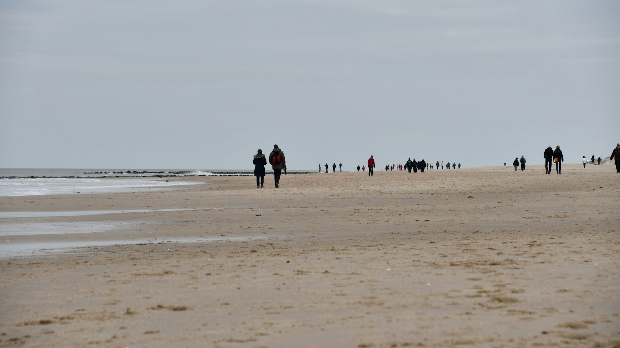 Spaziergänger sind am Montag bei bedecktem Himmel am Strand von Westerland unterwegs.