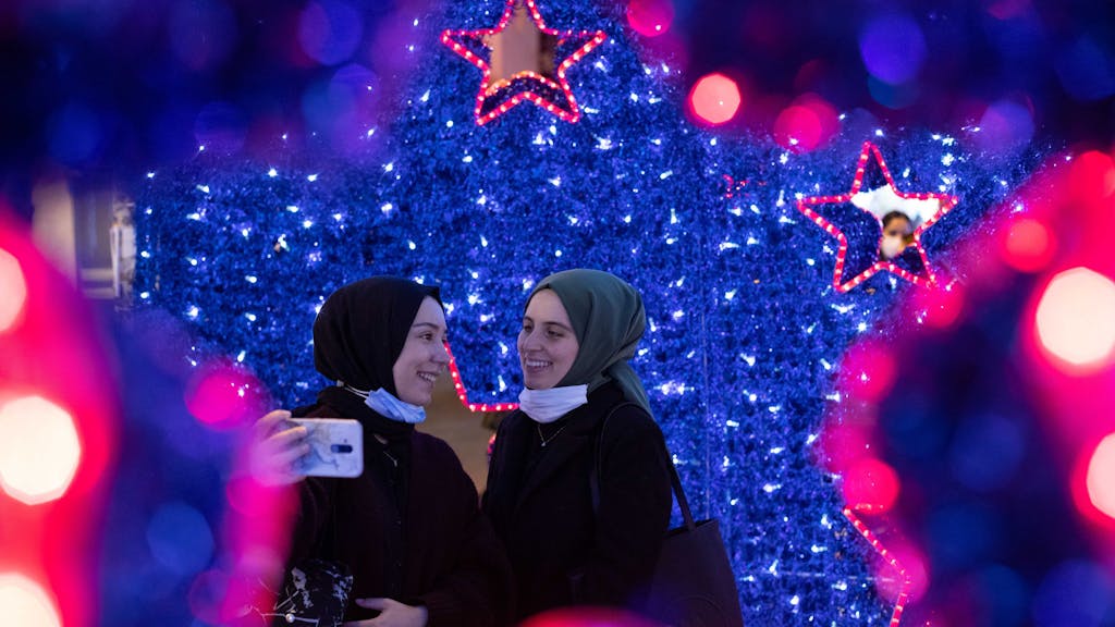 Zwei junge Mädchen machen ein Selfie vor Weihnachtssternen und Weihnachtsbeleuchtung auf dem Basarplatz von Kadikoy in Istanbul.