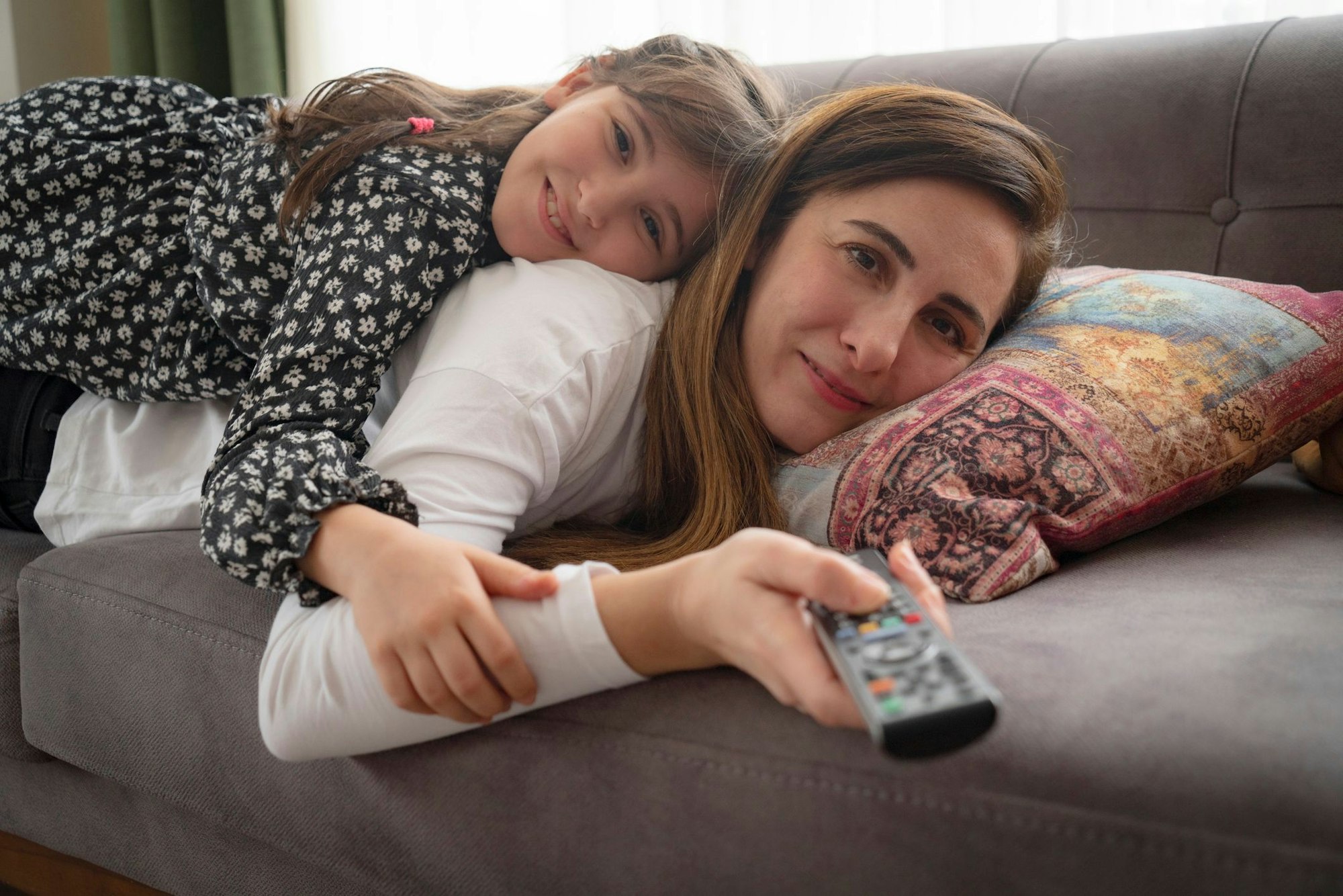 Mutter und kleine Tochter liegen auf dem Sofa und schauen Fernsehen