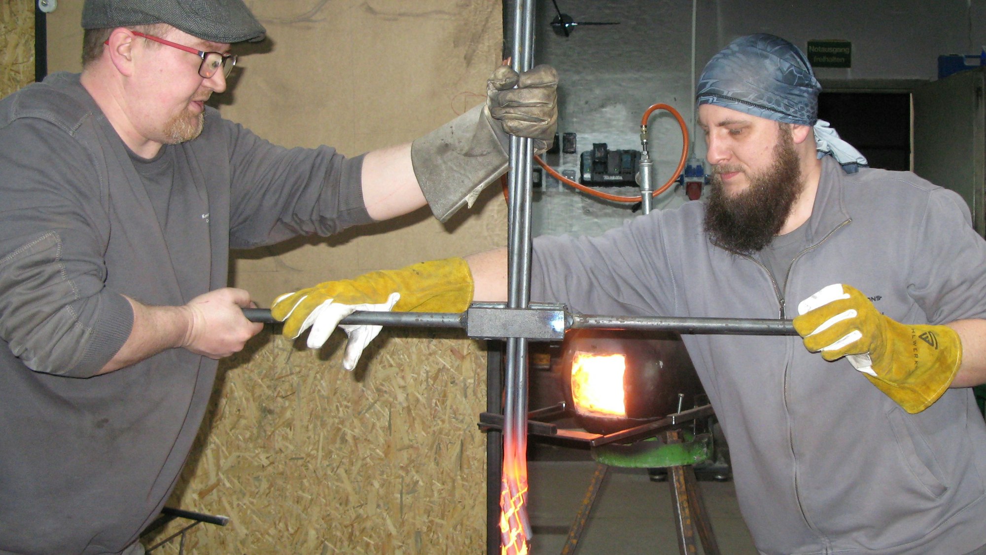 Die Metallbaumeister Deitenbach und Weber wendeln mit einer Stange glühende Stahlstangen.