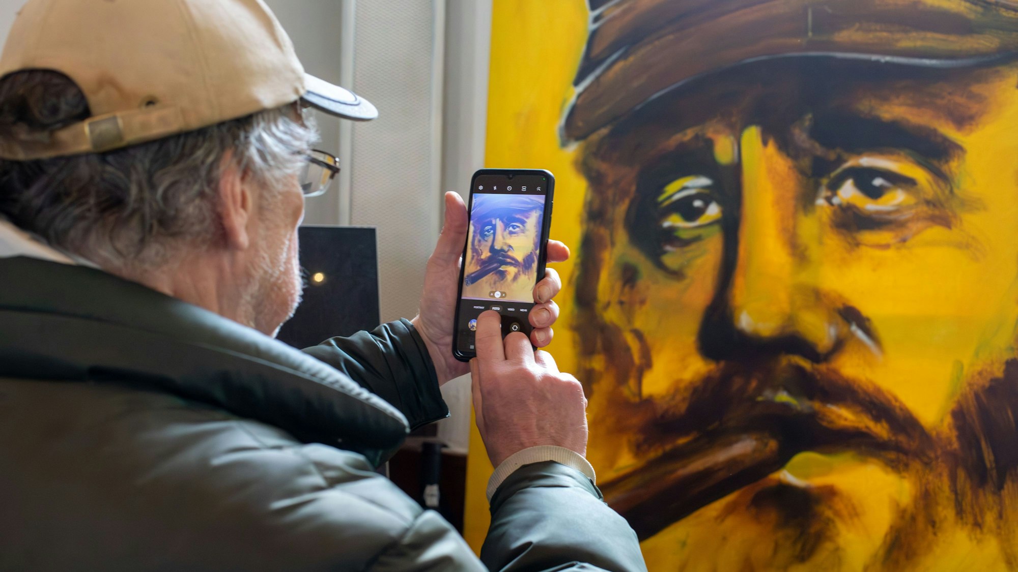 Ein Mann fotografiert mit dem Smartphone ein gemaltes Porträt von Fidel Castro.
