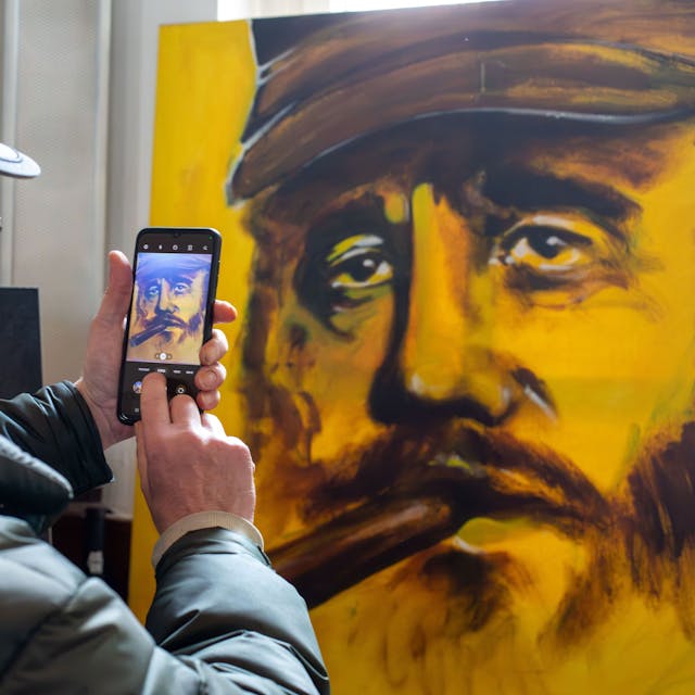 Ein Mann fotografiert mit dem Smartphone ein gemaltes Porträt von Fidel Castro.