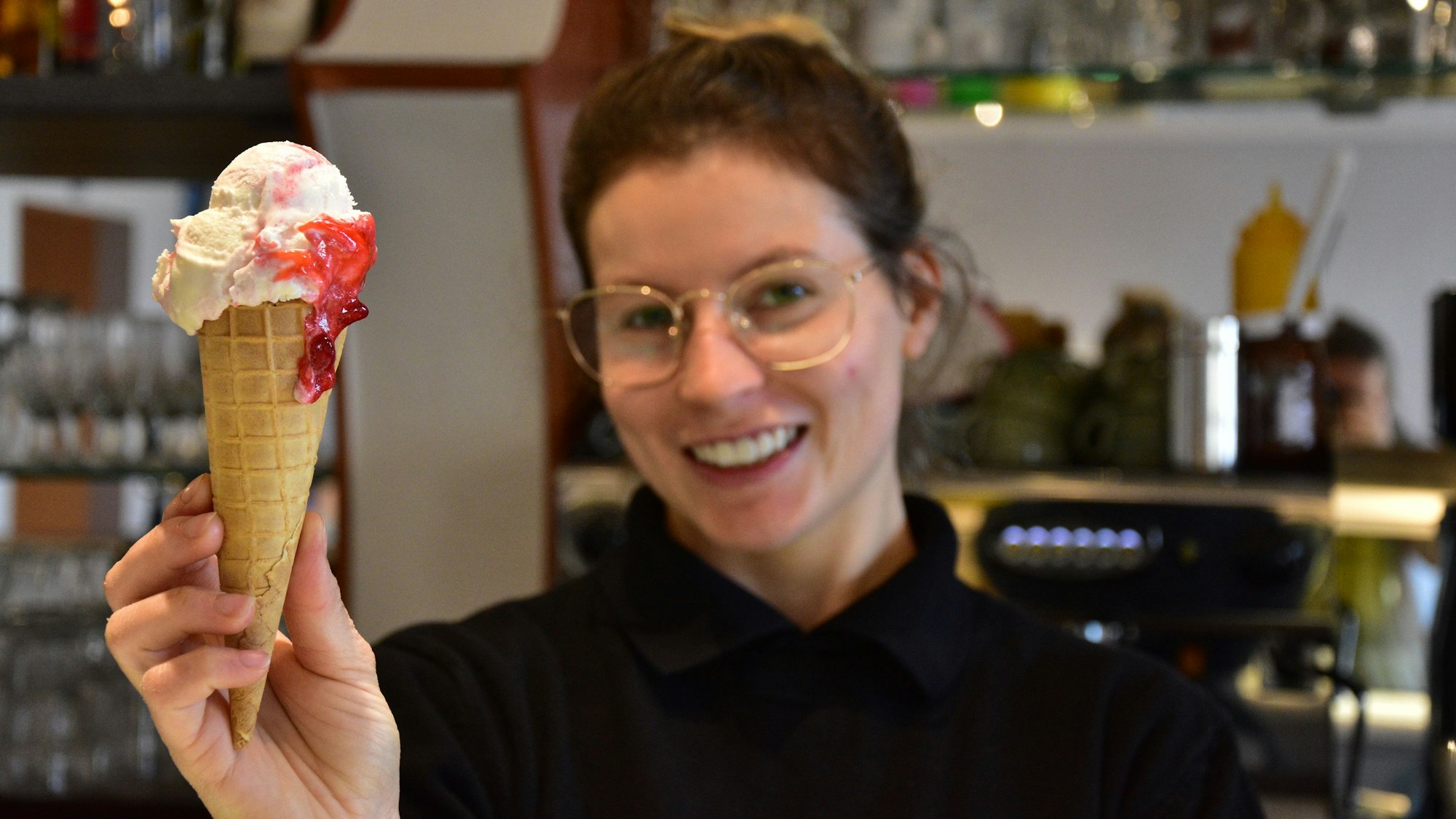 Kamilla Martins Cardoso serviert eine Eiswaffel im Eiscafé Darella in Sankt Augustin-Menden und lächelt dabei in die Kamera.