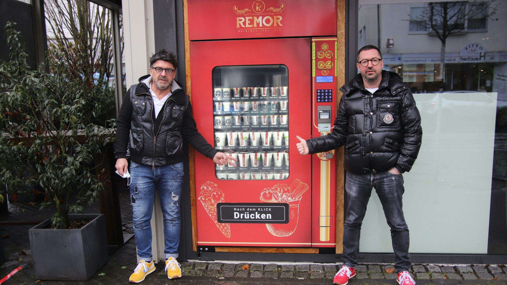 Die Brüder Rino und Massimo Remor verkaufen ihr selbstgemachtes Eis aus einem Eisautomaten heraus. Sie stehen beide davor und zeigen auf den Automaten.