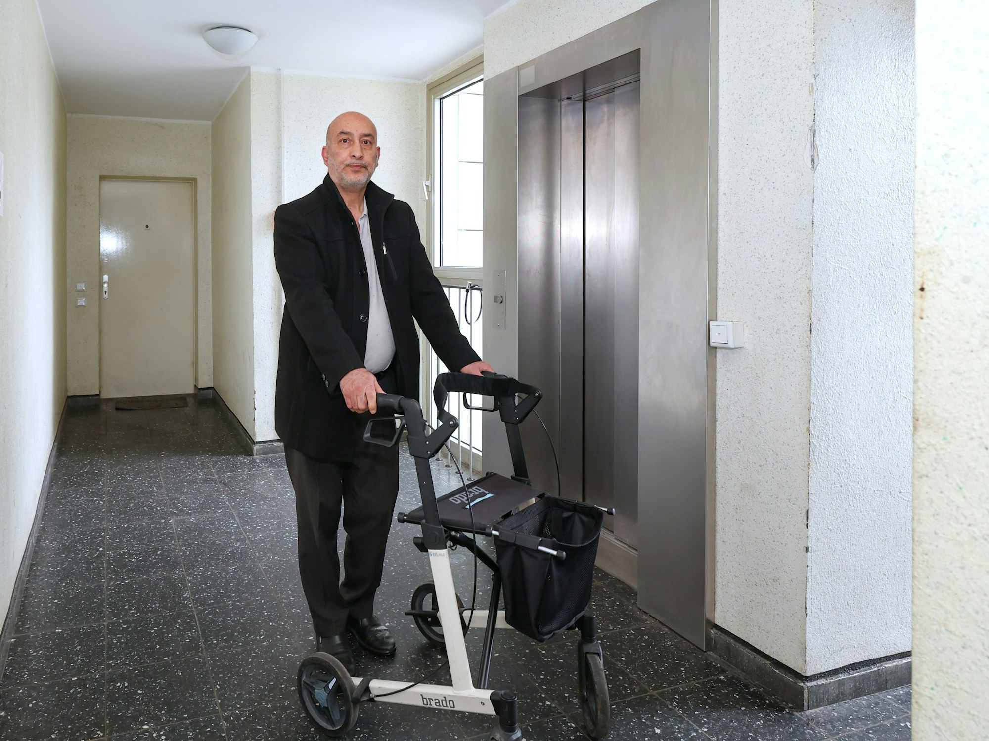 Ein Mann steht mit einem Rollator vor einem Aufzug.