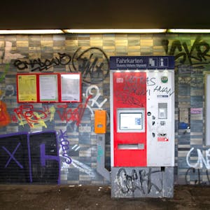 Eine gekachelte Wand in einem Bahnhof sowie ein Fahrkartenautomat und Fahrplanaushänge sind mit Graffiti und Schriftzügen beschmiert.&nbsp;