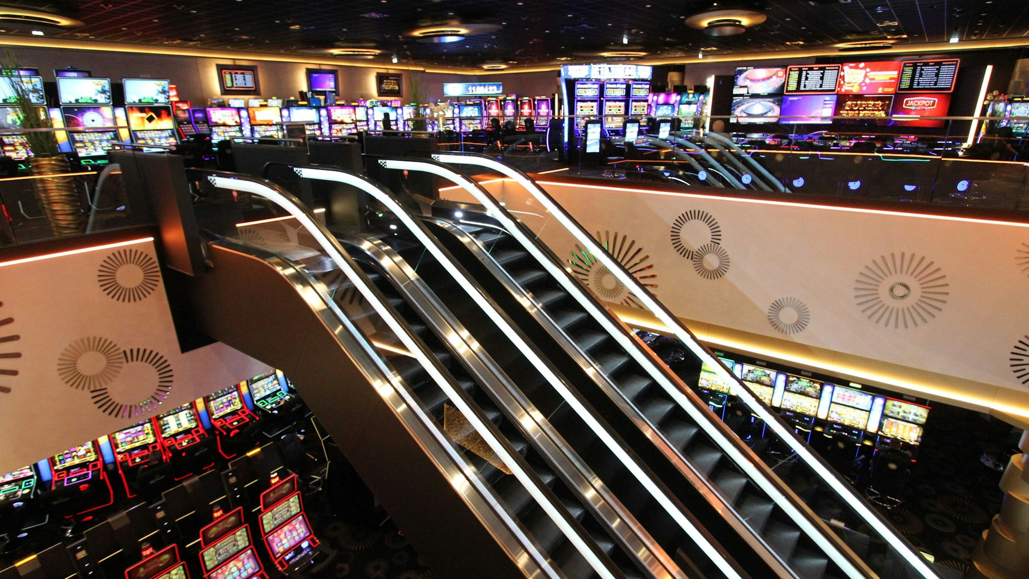 Blick in eine Spielbank mit vielen Automaten und zwei Rolltreppen