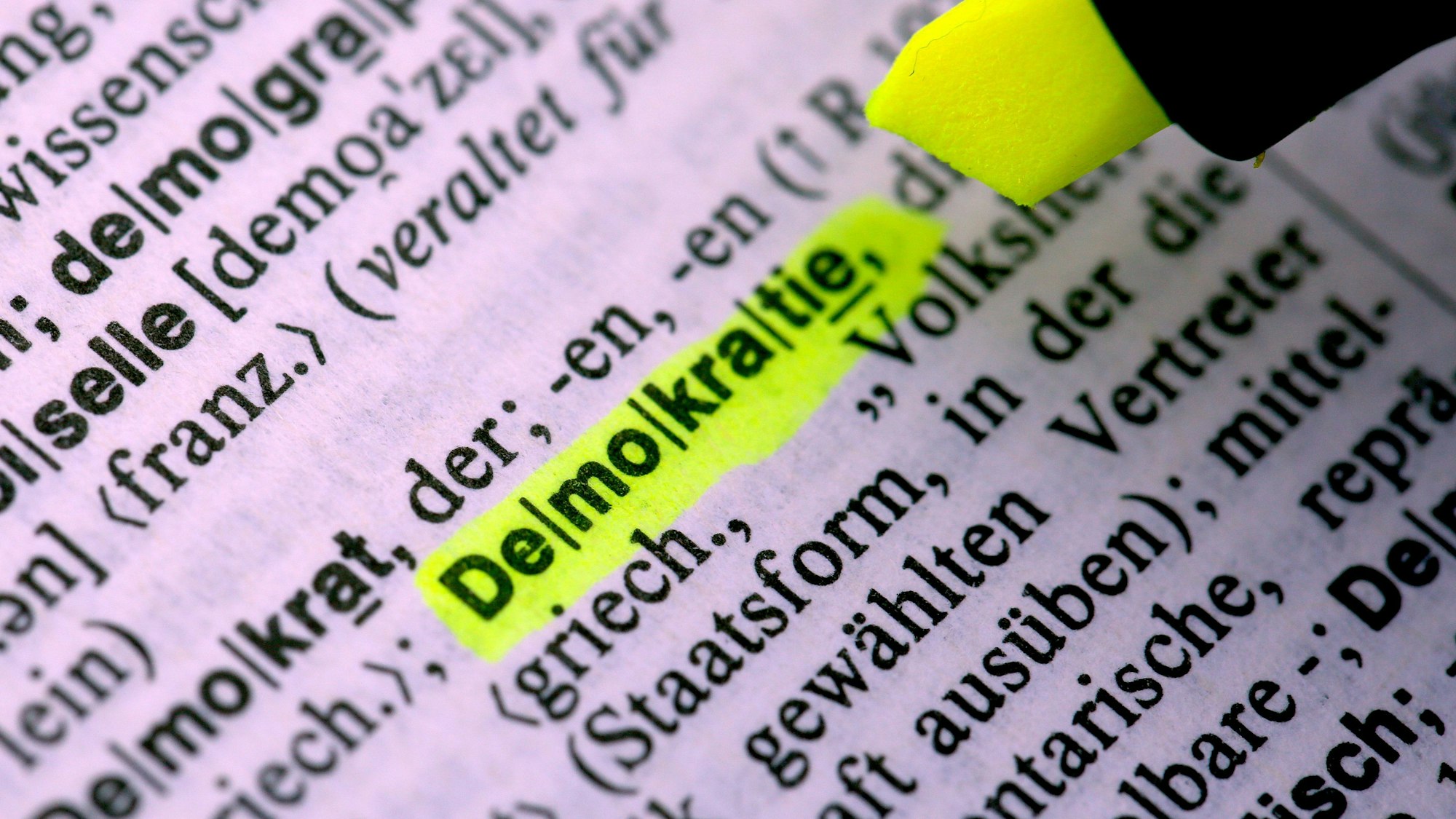 Das Wort „Demokratie“ wird in einem Duden mit einem gelben Textmarker markiert.