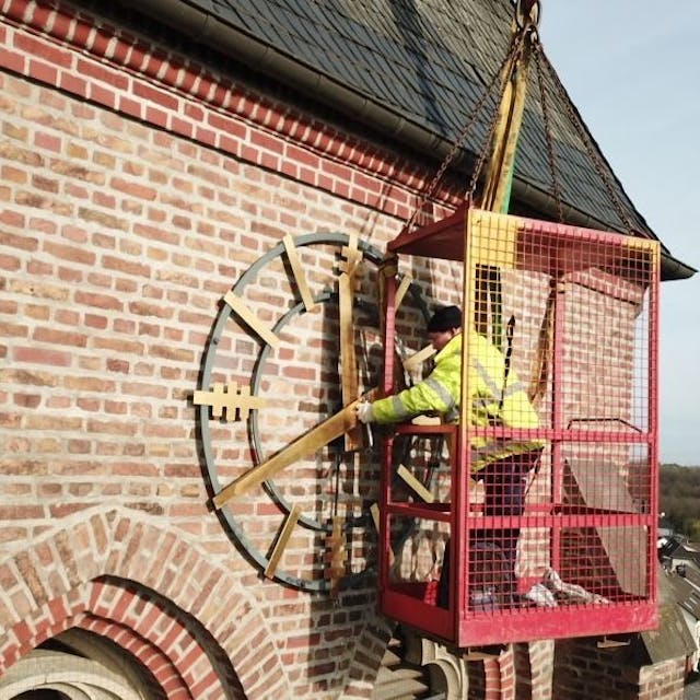 Zu sehen ist ein Arbeiter, der die goldene Kirchturmuhr repariert.