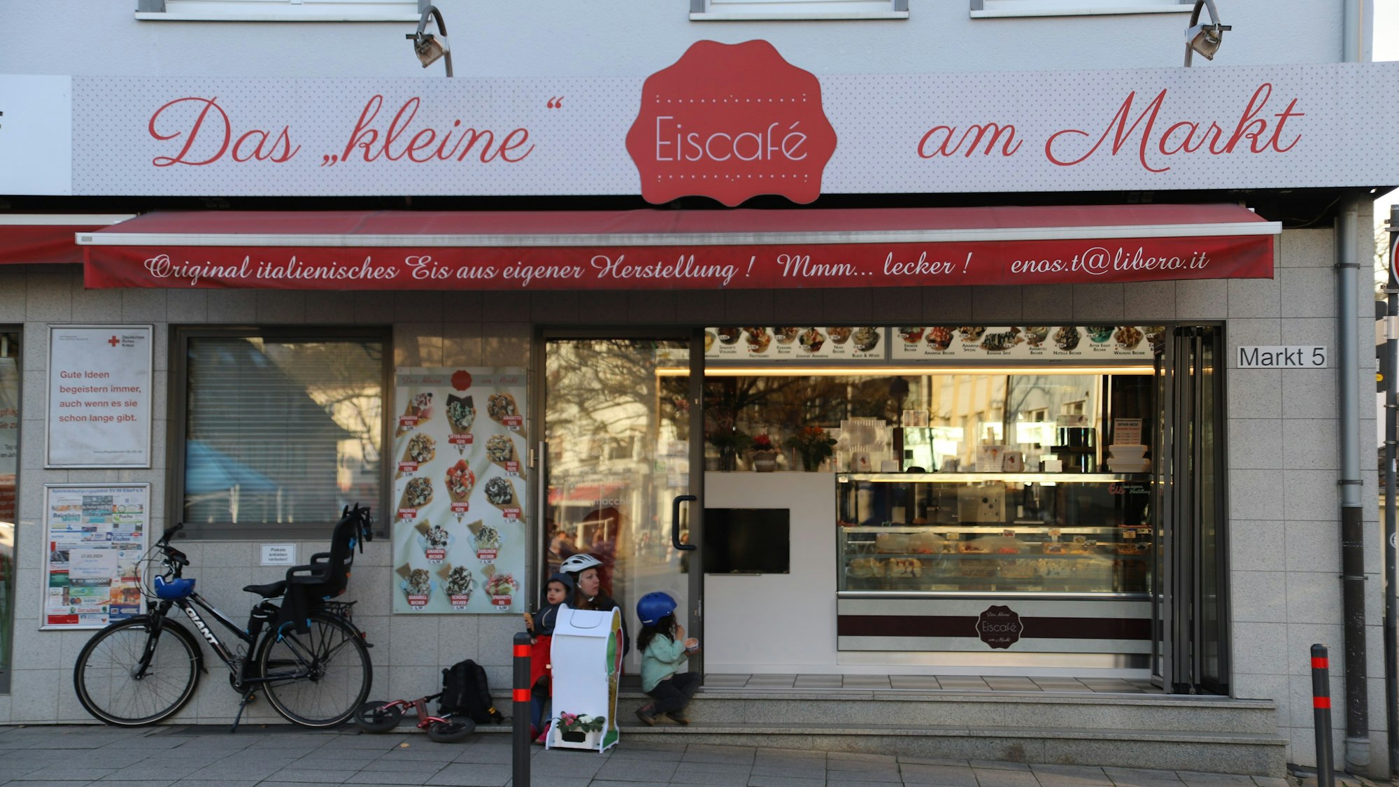 Das kleine Eiscafé am Markt in Eitorf in der Außenansicht. Links im Bild ist ein Fahrrad mit Kindersitz an die Hauswand gelehnt.