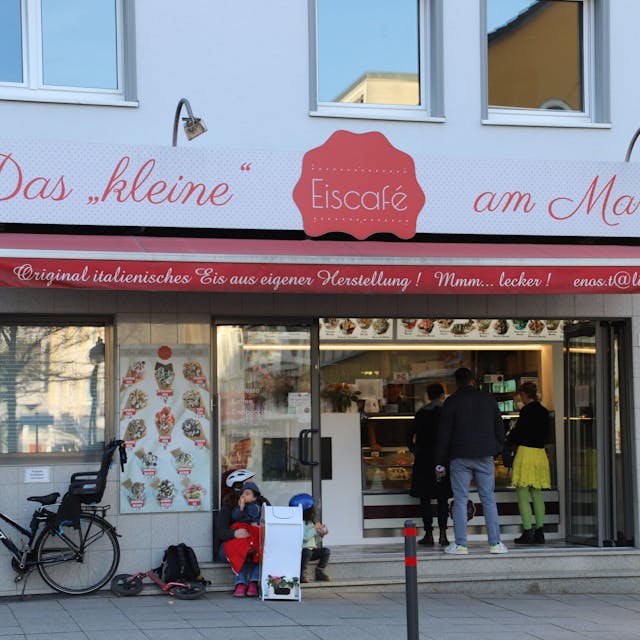 Das kleine Eiscafe am Markt in Eitorf in der Außenansicht. Menschen bestellen an der Eistheke, links im Bild ist ein Fahrrad mit Kindersitz an die Hauswand gelehnt.