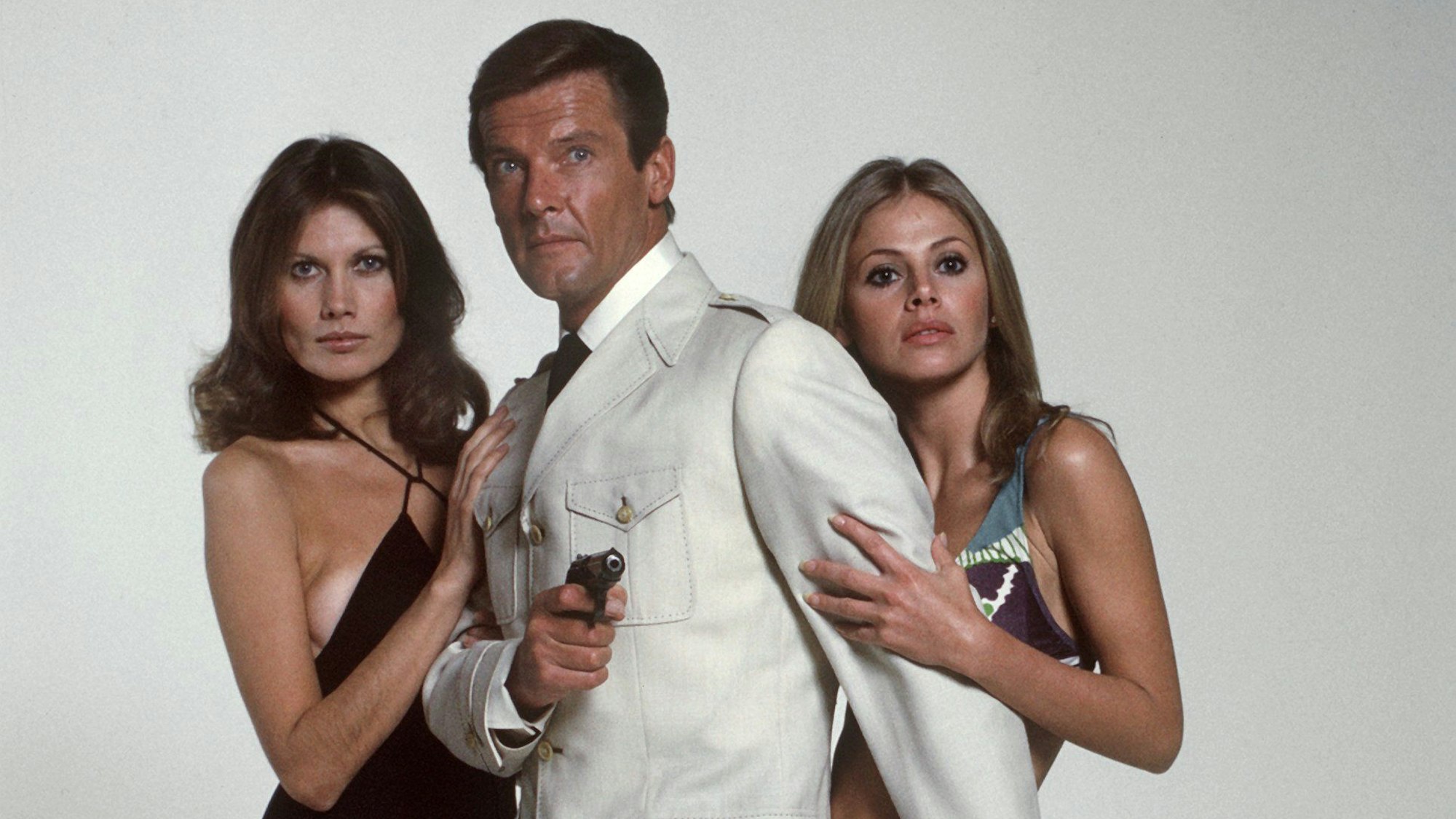 Das Archivbild von 1972 zeigt den dritten „James Bond“-Darsteller Roger Moore mit den Bond-Girls Maude Adams (l) und Britt Eklund im Film „Der Mann mit dem goldenen Colt“.