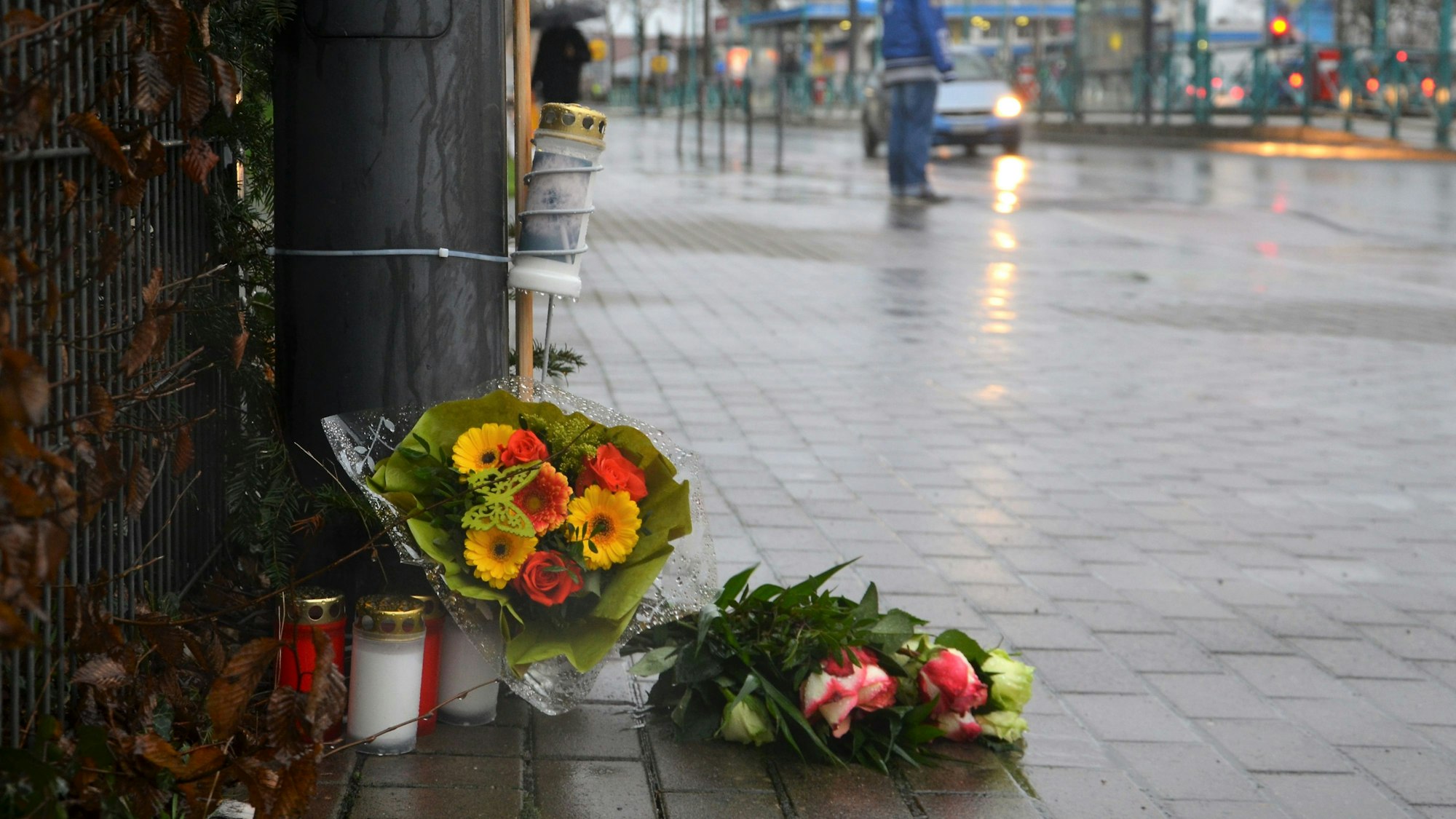 Kerzen und Blumen liegen auf der Siegburger Straße an der Stelle, wo ein Fußgänger im Januar 2023 von einem Auto überfahren wurde.