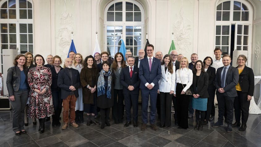 28 Frauen und Männer lächeln in die Kamera, Ministerpräsident Hendrik Wüst überragt sie alle.