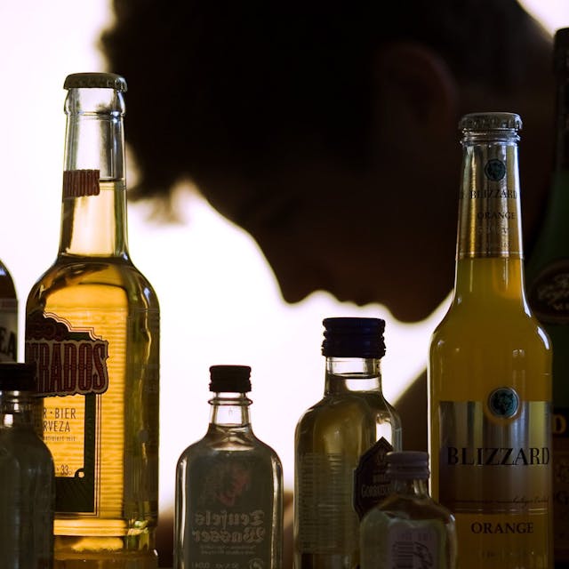 ARCHIV - ILLUSTRATION&nbsp;- Ein Jugendlicher sitzt hinter Flaschen mit Alkohol.