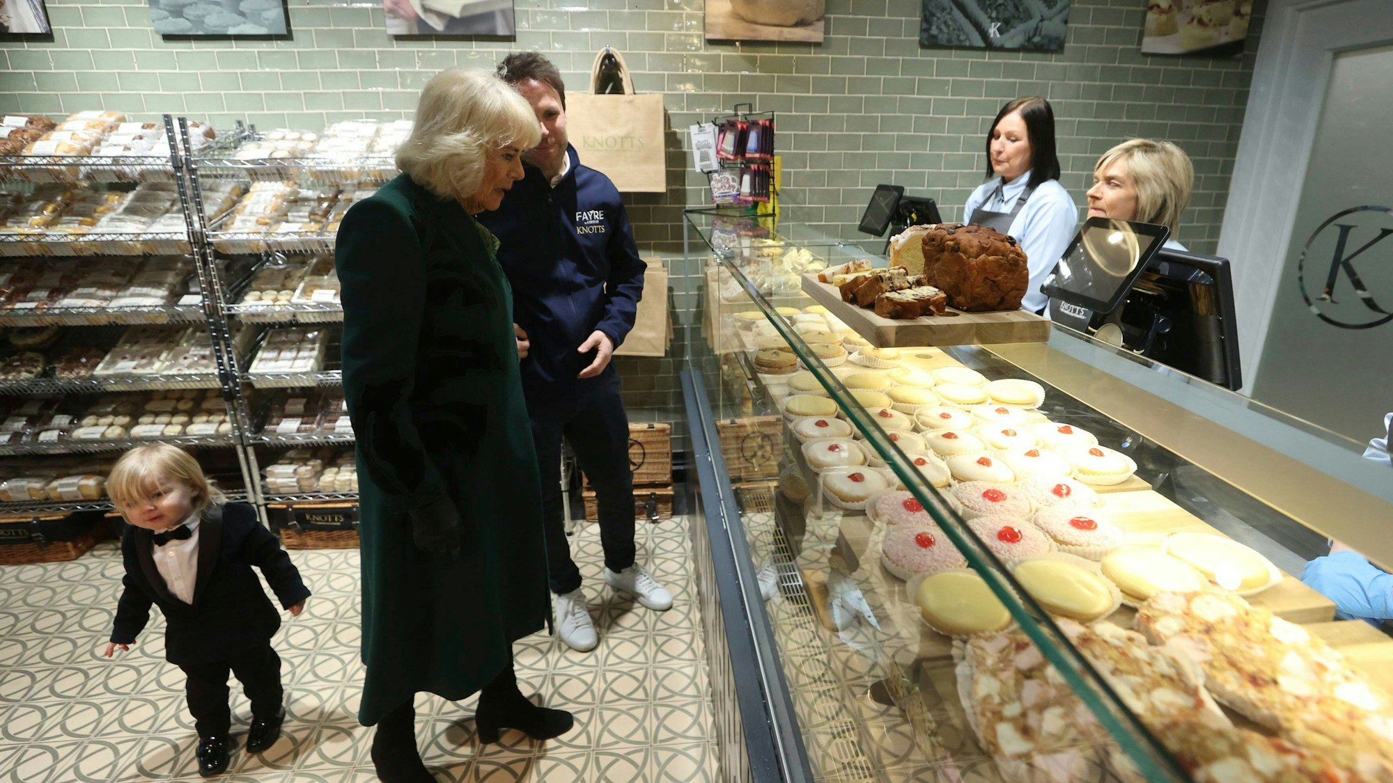 Königin Camilla (m) trifft den Besitzer der Knotts Bakery, William Corrie, mit seinem Sohn Fitz (l) bei einem Besuch in der Lisburn Road in Belfast.