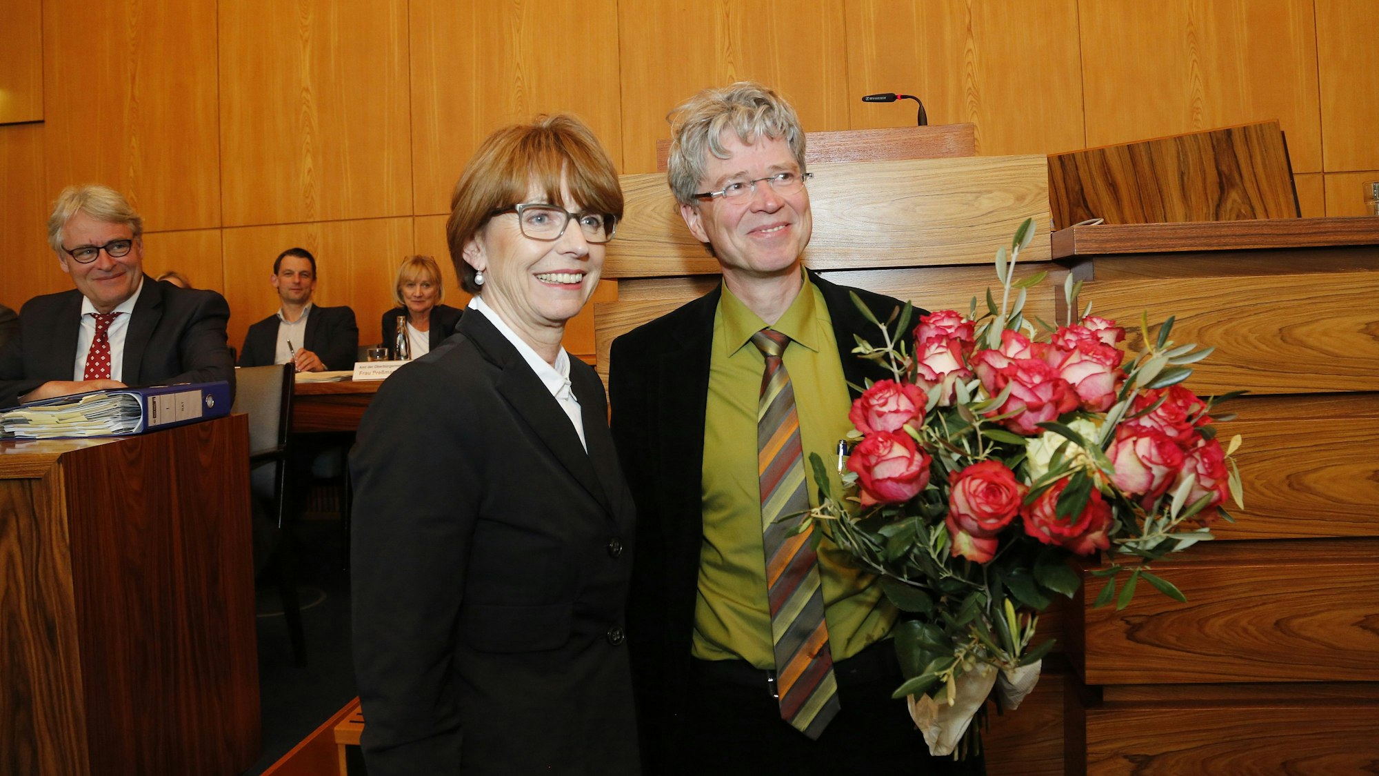 Das Bild zeigt eine Frau und einen Mann im Kölner Ratssaal, er hält einen Blumenstrauß in der Hand.