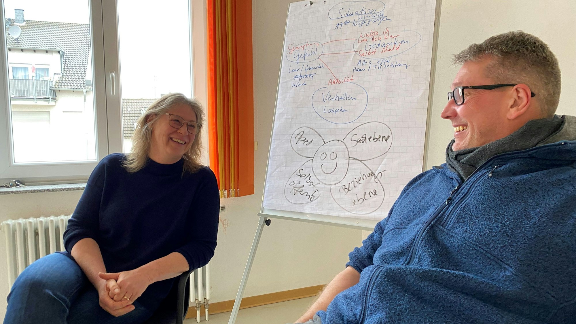 Maria Surges-Brilon und Frank Commer von der Euskirchener Caritas-Beratung sitzen neben einer Tafel, auf der Notizen im Rahmen des niederländischen Skoll-Programmes gemacht wurden.