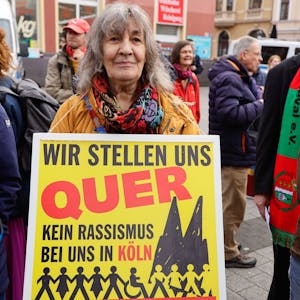 Menschen bei einer Demonstration. Eine Frau trägt ein Plakat mit der Aufschrift: „Wir stellen quer - Kein Rassismus bei uns in Köln“.&nbsp;