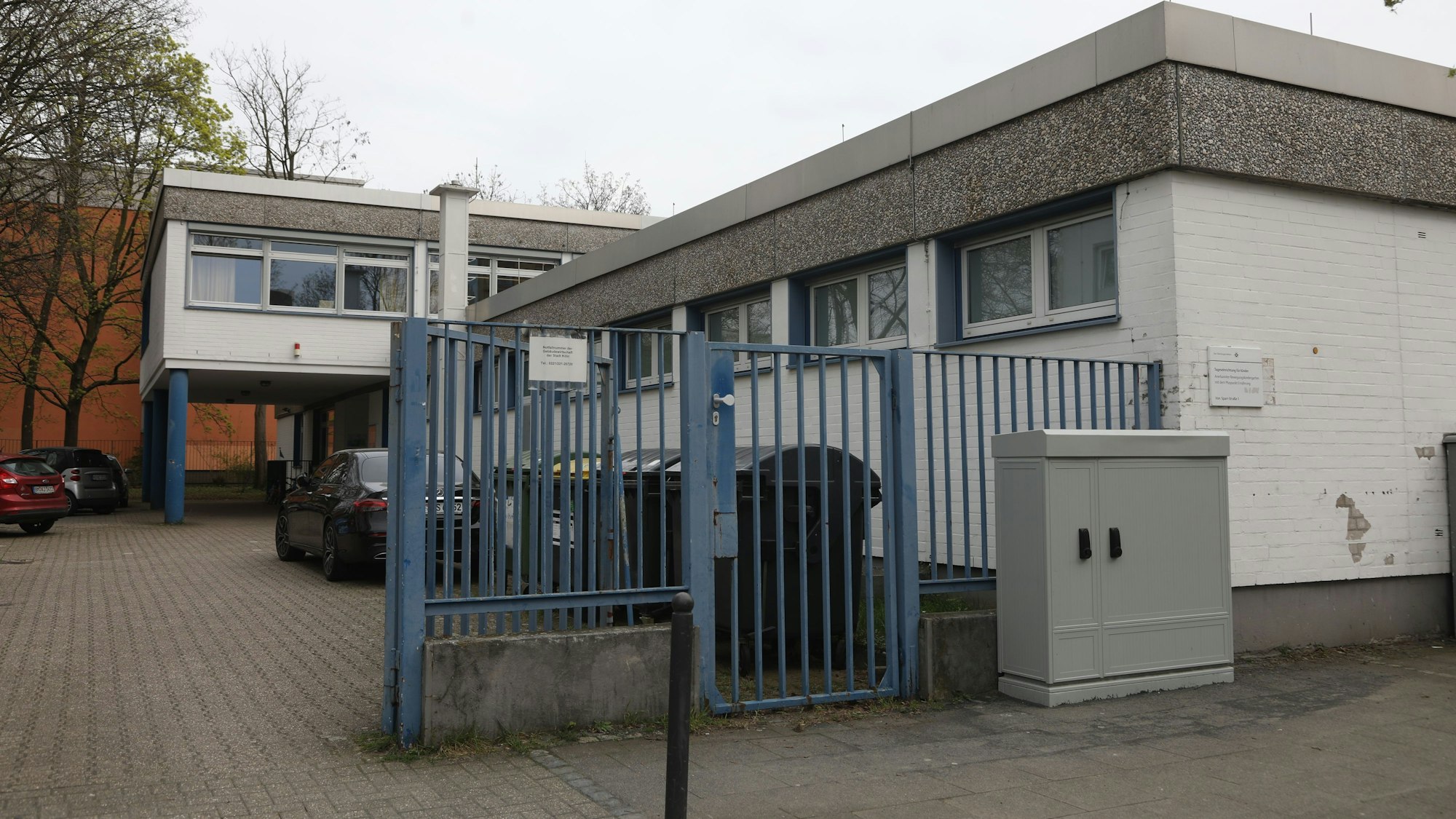 Zu sehen ist eine Kölner Kindertagesstätte von außen mit einem blauen Tor im Vordergrund.