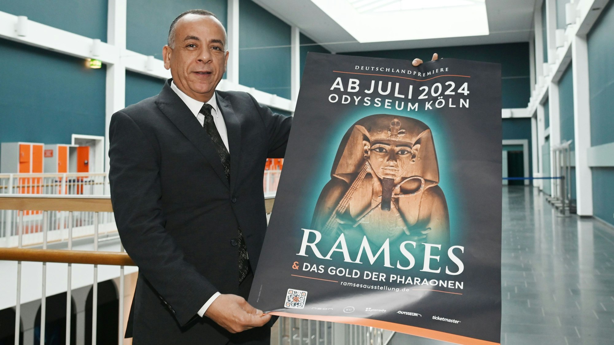 Mostafa Waziri hält in den Gängen des Odysseums Köln ein Plakat der Ausstellung "Ramses & Das Gold der Pharaonen". Die Ausstellung ist ab 13. Juli 2024 zu Gast im Odysseum. Dr. Mostafa Waziri hat sich vor Ort ein Bild gemacht.