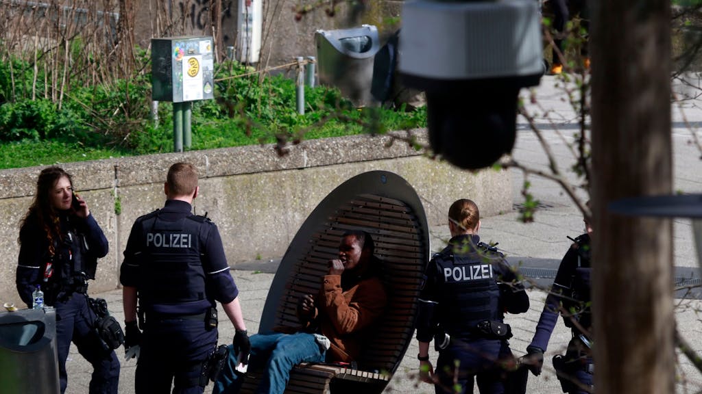 Ein Mann sitzt am Ebertplatz, drei Einsatzkräfte der Polizei stehen vor und neben ihm.